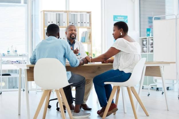 A dark-skinned doctor discussing preimplantation genetic testing PGT/PGD options with a Black couple in a modern fertility clinic.