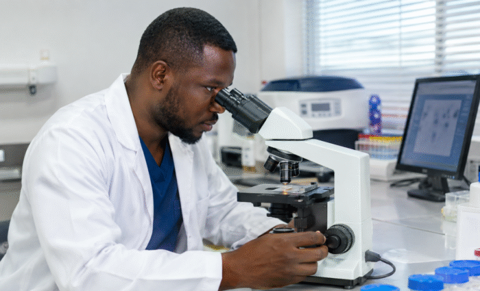 A male laboratory technician examining a semen analysis specimen under a microscope in a modern fertility clinic laboratory, representing where to do semen analysis in Akure.